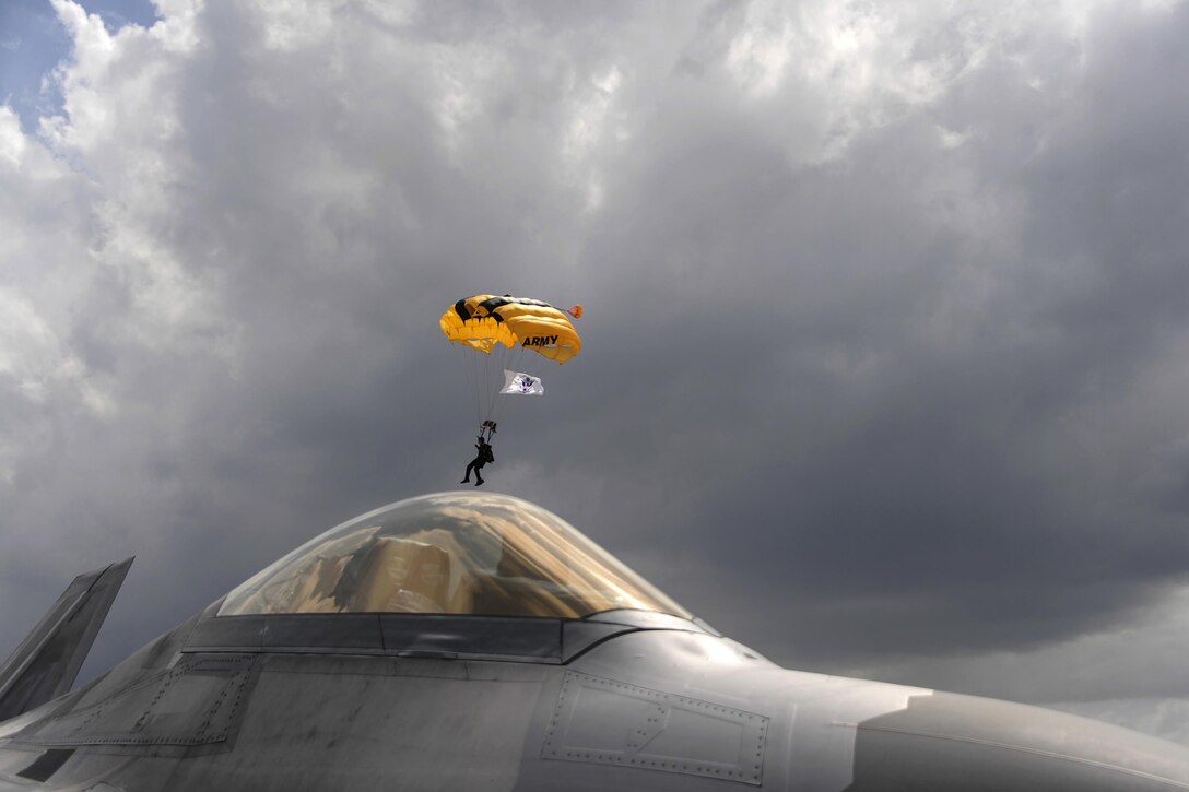 An Army Golden Knights parachute team member descends in the distance as an Air Force F-22 Raptor sits parked at Coast Guard Air Station Miami in Opa-locka, Fla., May 26, 2017, during the National Salute to America’s Heroes Air and Sea Show. Air Force, Army, Navy, Marine Corps and Coast Guard service members participated in the event. Air Force photo by Senior Airman Erin Trower