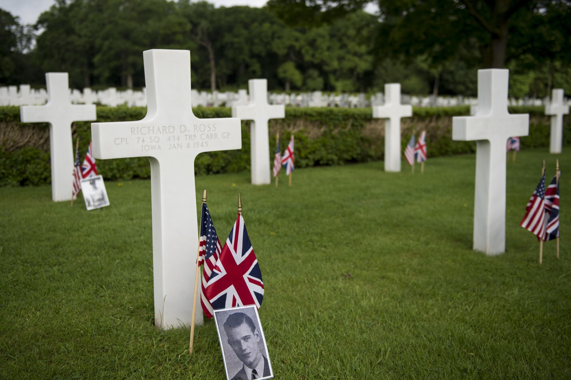 A photo of Army Air Corps Cpl. Richard Ross from the 74th Squadron 434th Troop Carrier Group sits in front of his marble cross headstone at the Cambridge American Cemetery in Cambridge, England May 29, 2017. Ross’s unit was part of the lineage that later transformed to the 434th Air Refueling Wing at Grissom Air Reserve Base, Indiana. (U.S. Air Force photo/Tech. Sgt. Benjamin Mota)