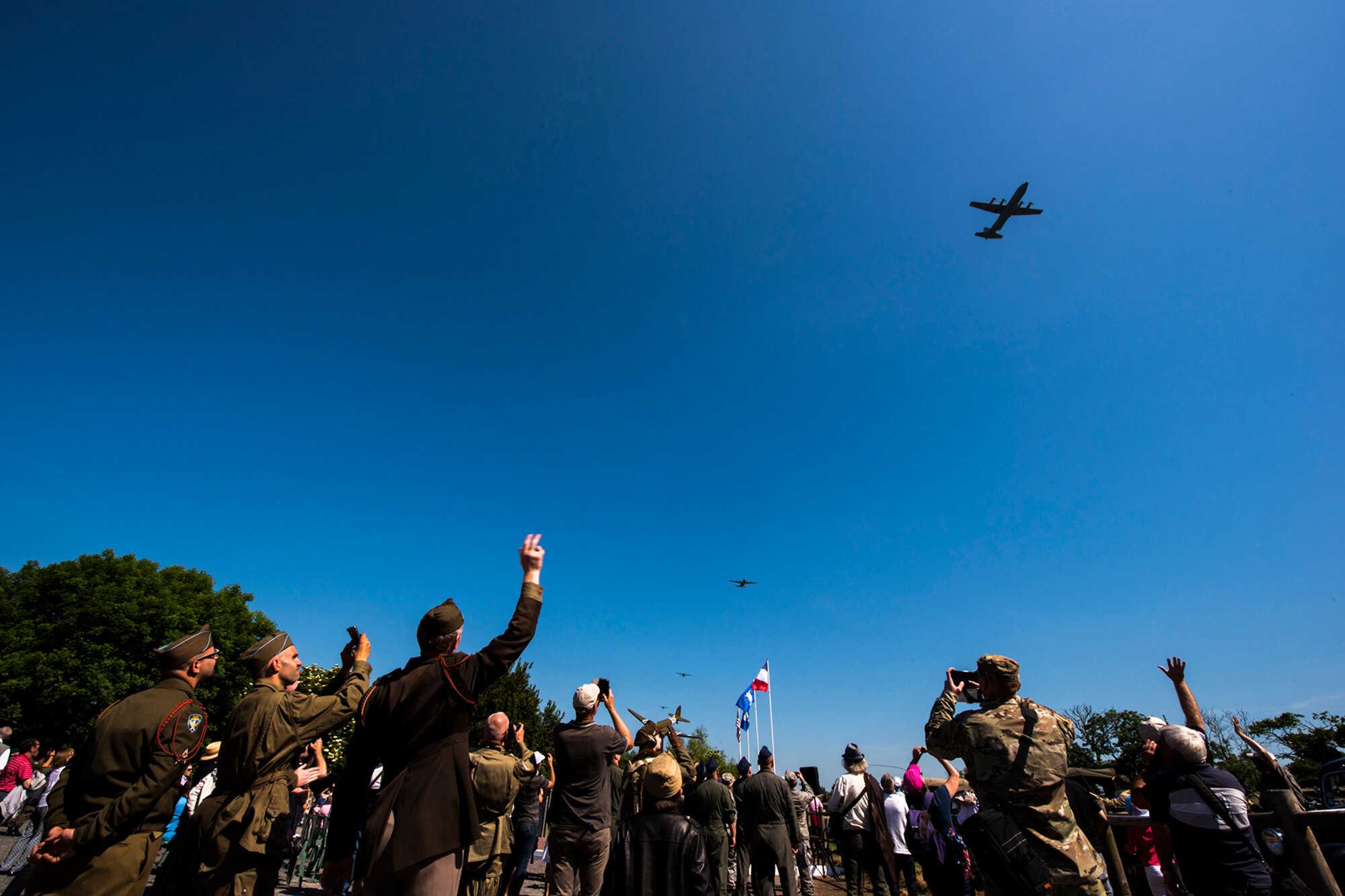Attendees wave to U.S. Air Force C-130J Super Hercules aircraft assigned to Ramstein Air Base, Germany, as the aircraft pass over Picauville, France, during a D-Day remembrance ceremony at the United States Army Air Forces Transport Memorial June 1, 2017. This event commemorates the 73rd anniversary of D-Day, the largest multinational amphibious landing and operational military airdrop in history, and highlights the U.S.' steadfast commitment to European allies and partners. Overall, approximately 400 U.S. service members from units in Europe and the U.S. are participating in ceremonial D-Day 73 events from May 31-June 7, 2017. (U.S. Air Force photo by Senior Airman Devin Boyer)