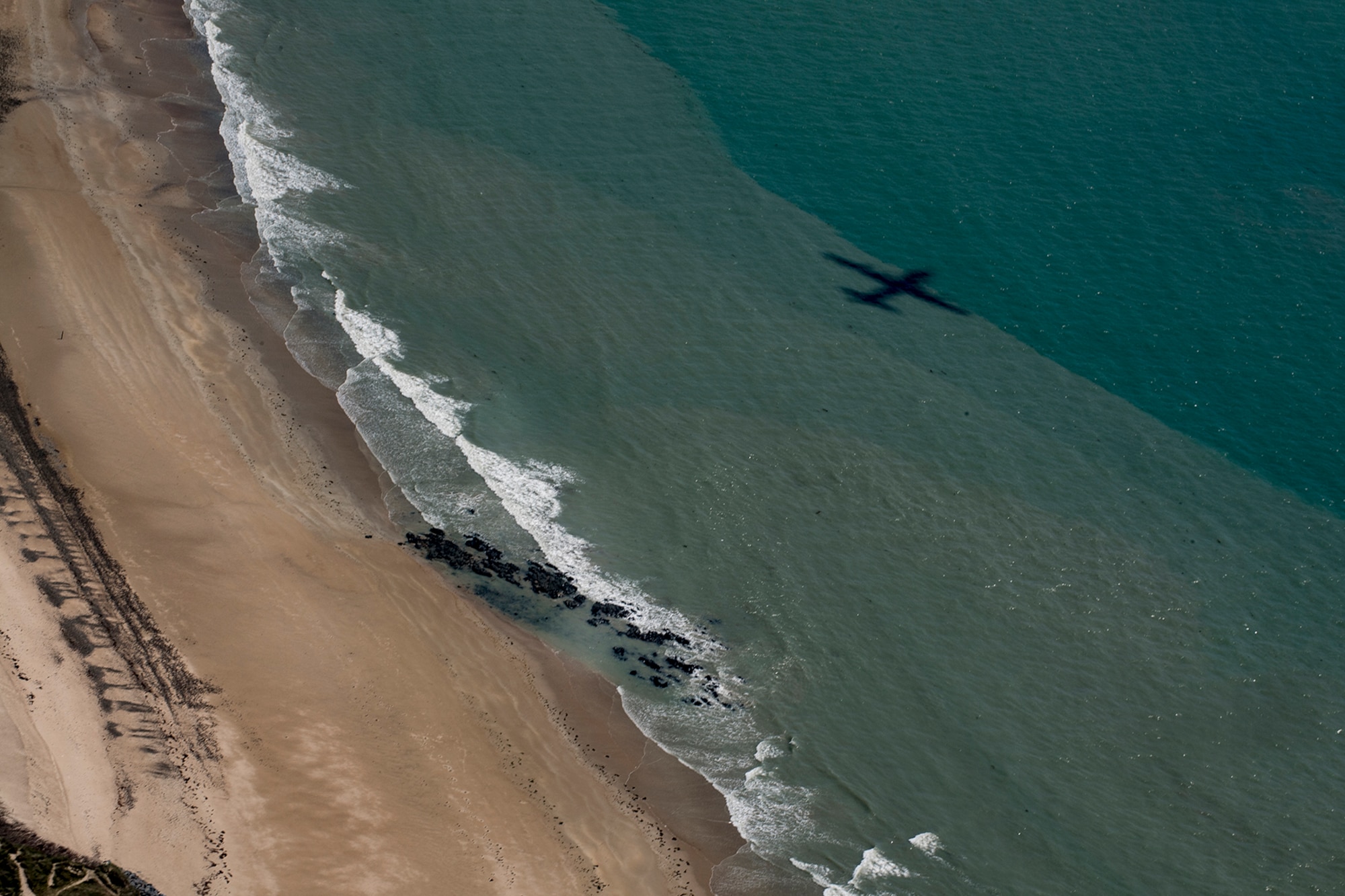 A U.S. Air Force C-130J Super Hercules assigned to the 37th Airlift Squadron at Ramstein Air Base, Germany, casts its shadow over the beaches of Normandy during a flyover in France, June 2, 2017. This event commemorates the 73rd anniversary of D-Day, the largest multinational amphibious landing and operational military airdrop in history, and highlights the U.S.' steadfast commitment to European allies and partners. Overall, approximately 400 U.S. service members from units in Europe and the U.S. are participating in ceremonial D-Day 73 events from May 31-June 7, 2017. (U.S. Air Force photo by Senior Airman Devin Boyer)