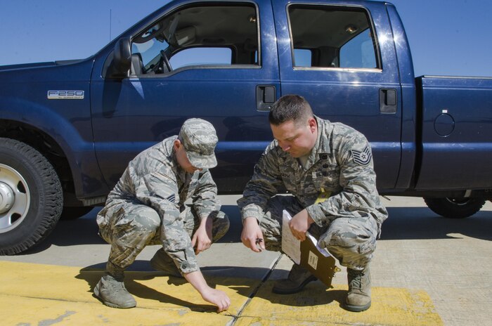 SrA Mike Vasilakos Engineering Assistant, 108th Civil Engineer Squadron, and Tech. Sgt. Sean Joseph, Operations Manager, 108th Civil Engineer Squadron, inspect and document a crack in the cement of the 108th aircraft parking ramp that without proper maintenance has the potential to create FOD (foreign object debris) and damage an aircraft. (U.S. Air National Guard photo by Staff Sgt. Ross A. Whitley/Released)