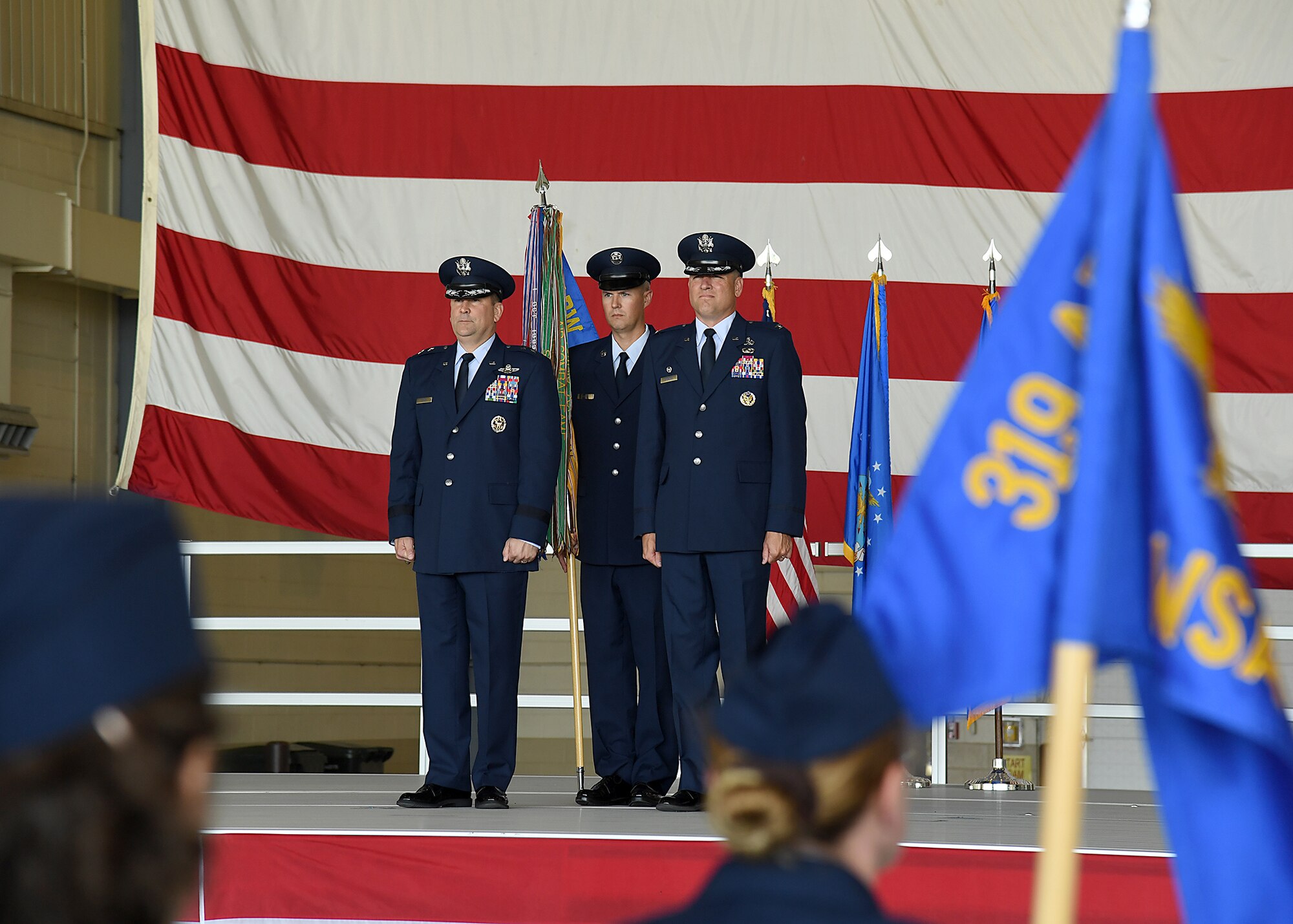 Maj. Gen. Christopher Bence, U.S. Air Force Expeditionary Center commander, left, and Col. Benjamin Spencer, 319th Air Base Wing commander, right, stand in preparation to pass the 319 ABW guidon. Chief Master Sgt. Brian Thomas, 319 ABW command chief, center, provided the guidon for the symbolic exchange during the wing Assumption of Command ceremony June 6, 2017, on Grand Forks Air Force Base, N.D. Spencer and Thomas bring a two-year working relationship to the wing as they take over leading the Warriors of the North. (U.S. Air Force photo by Senior Airman Ryan Sparks)