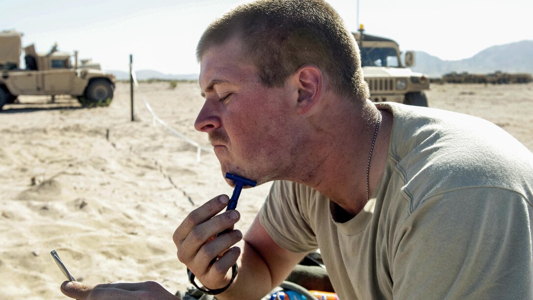 Army Spc. John Gore uses a disposable razor, a pocket mirror and bottled water to shave in the Mojave Desert during training at the National Training Center at Fort Irwin, Calif., June, 5, 2017. Gore is assigned to the 2nd Battalion, 114th Field Artillery Regiment. Mississippi National Guard photo by Sgt. Edward Lee