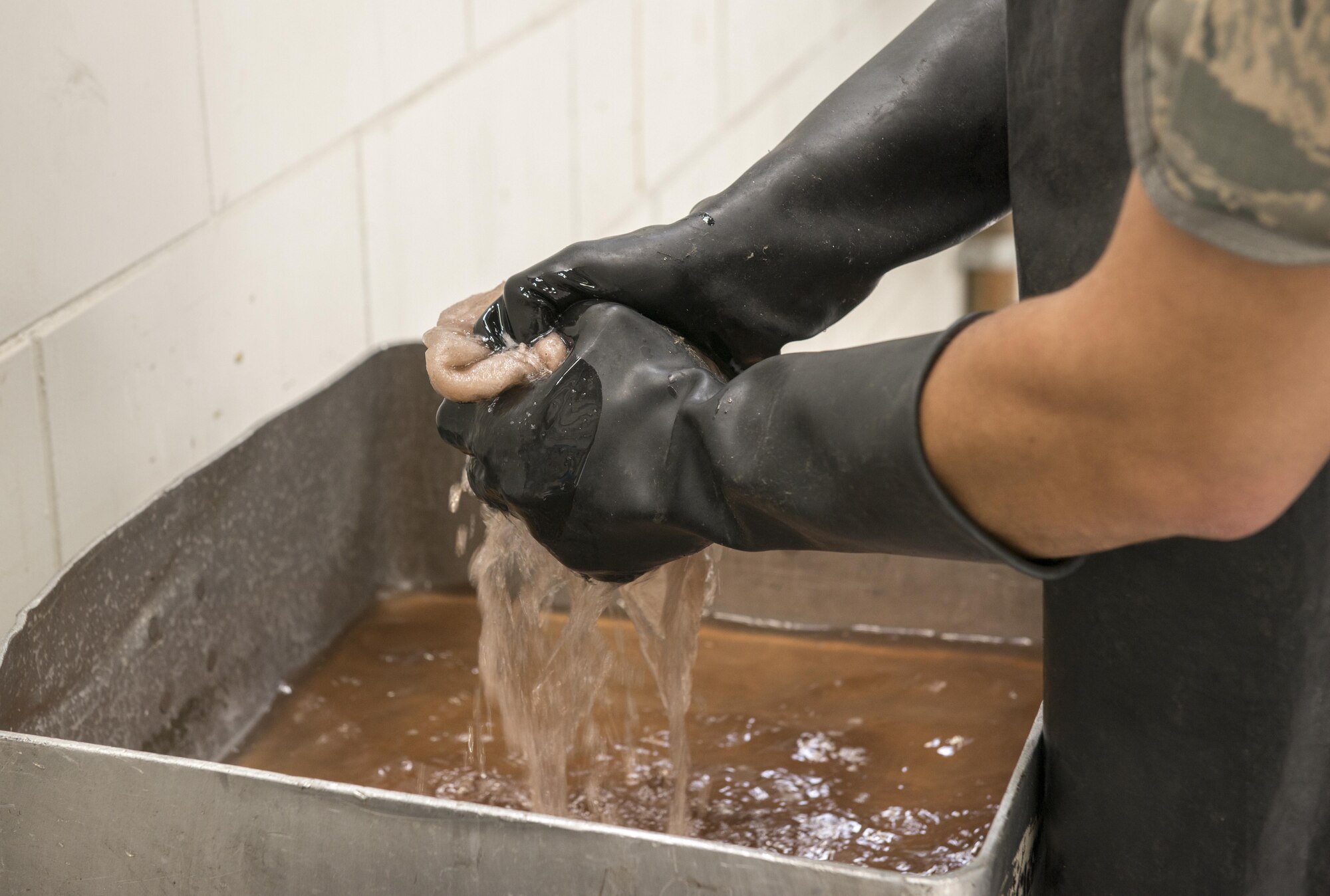 U.S. Air Force Airman 1st Class Steven Melo-Justo, 7th Equipment Maintenance Squadron aerospace ground equipment craftsman, wrings diesel from a fuel-contaminated absorbent at Dyess Air Force Base, Texas, May 10, 2017. After fuel-contaminated absorbents are containerized in a drum, the drum is taken to a 90-day facility where any remaining fuel is removed from the absorbents using a centrifuge.  Afterwards, the absorbents can be re-used several more times prior to being properly disposed of, saving the Air Force money for both disposal and purchase of new absorbents. The fuel removed from the absorbents is recycled off-base at no cost to the government. (U.S. Air Force photo by Senior Airman Austin Mayfield)