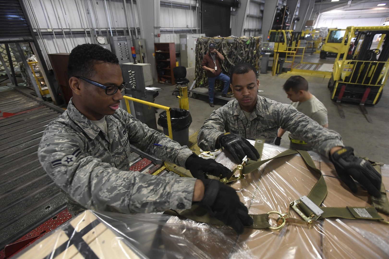 Airman 1st Class Isaiah Reed and Airman 1st Class Ryan Davila, 305th Aerial Port Squadron cargo processors, strap down a cargo pallet in the Aerial Port warehouse at Joint Base McGuire-Dix-Lakehurst, New Jersey, June 2, 2017. The cargo prepared here typically finds its way to Ramstein Air Base before being disseminated to installations around the world. 