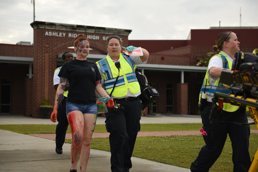 Members of Dorchester County Emergency Medical Services escort a moulage volunteer from the Ashley Ridge High School cafeteria during a mass casualty exercise in Summerville, S.C., June 6, 2017. Joint Base Charleston assisted multiple Dorchester County emergency response agencies during the community partnered exercise. The event aimed to improve interagency communication and response to large scale emergencies.