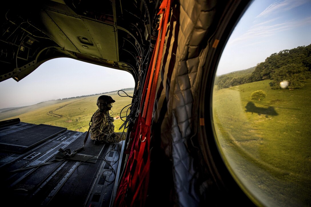 An Air Force loadmaster sits on the ramp of a Chinook helicopter flying over the Cincu Training Area in Romania, June 6, 2017, during training with British Grenadier Guards. Allied Joint Force Command Naples courtesy photo