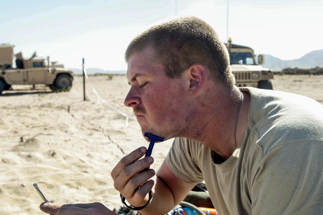 Army Spc. John Gore uses a disposable razor, a pocket mirror and bottled water to shave in the Mojave Desert during training at the National Training Center at Fort Irwin, Calif., June, 5, 2017. Gore is assigned to the 2nd Battalion, 114th Field Artillery Regiment. Mississippi National Guard photo by Sgt. Edward Lee