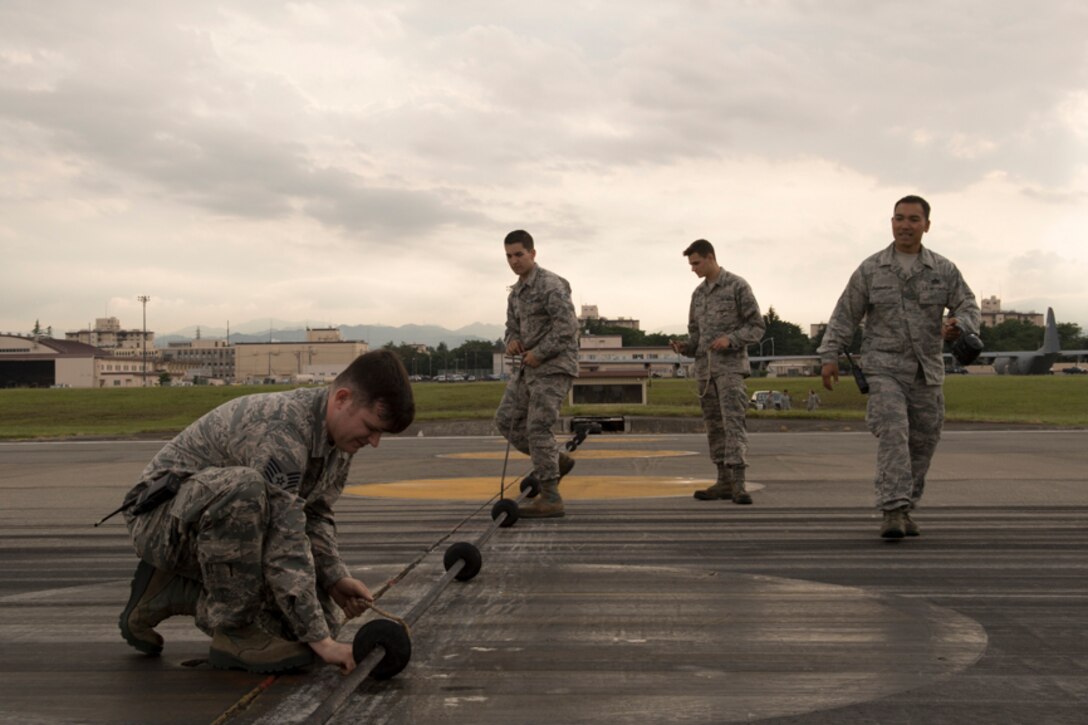 Airmen with the 374th Civil Engineer Squadron power productions shop inspect an emergency aircraft landing cable on the runway at Yokota Air Base, Japan, June 1, 2017, during an annual certification test of Aircraft Arresting System. Testing the system on an annual basis is the responsibility of the 374 CES and 374th Operations Support Squadron airfield management. (U.S. Air Force photo by Yasuo Osakabe)