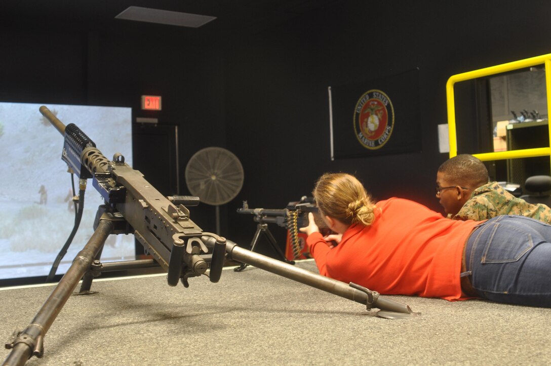 Julia Blair fires an M-249 at the Indoor Simulated Marksmanship Trainer alongside husband, Cpl. Omri Blair.