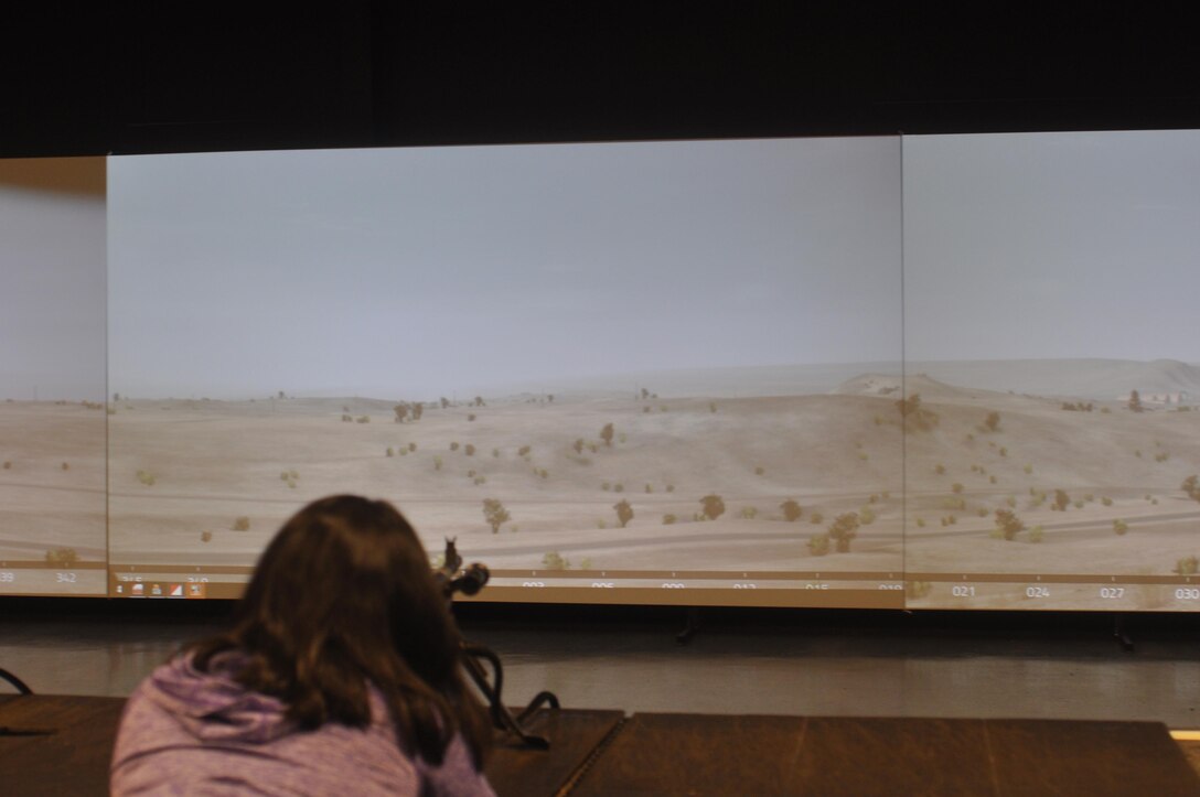 A spouse at the Indoor Simulated Marksmanship Trainer, or as Marines call it "A video game on steriods" is able to practice shooting military weapons. The simulator cuts costs by eliminating the need for ammo during practice.
