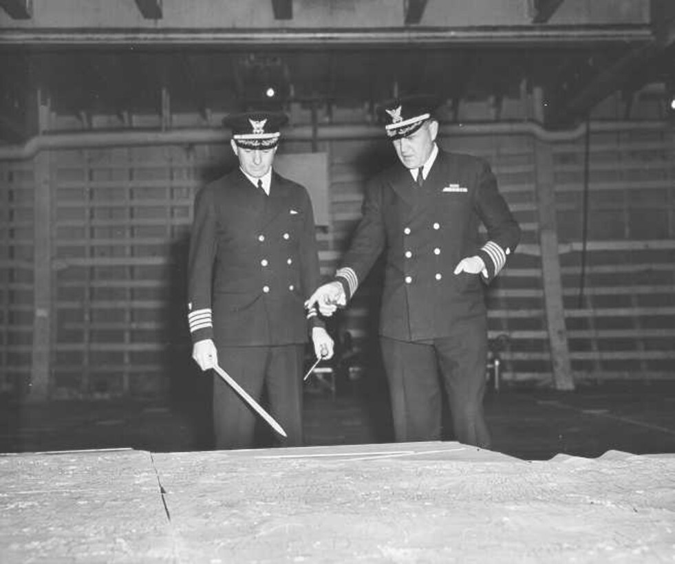 Coast Guard Captains Edward Fritzche (left) and Miles Imlay (right) discuss the invasion of Omaha Beach on a relief map laid out in the hold of the Samuel Chase.

Officer uniform: standard Navy-issue dress blues with Coast Guard devices on sleeves and hats.