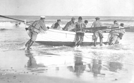 Nauset Life-Saving crew launching their surfboat, all wearing mixed uniforms with wading boots and cork life vests; no date, possibly post-1915 era.