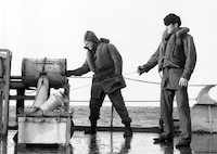 Winter clothing, kapok life vests.  Coast Guardsman on right is wearing the standard Navy issue watch cap.   
They are preparing to fire a "K" gun depth charge projector.
