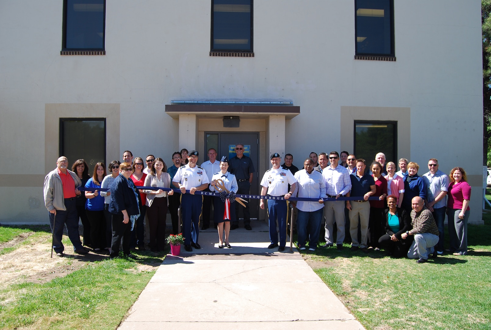 Air Force Col. Alice W. Treviño, Defense Contract Management Agency Western Region commander, is joined by DCMA Albuquerque employees as she cuts the ribbon to officially open building 20200B, DCMA Albuquerque’s new Kirtland Air Force Base office facility. From left: Denise Ulibarri, Brittney Volk, Craig Jones, Lisa Solis, Sean Anderson, Wade McVey, Mary Trimbell, Kelly Smith, Jon Gonzales, Stephanie Vigil, David Romero, Debora Santillan, Army Col. Robert Miceli, Vicki Strause, George Allen, Joe Hernandez, Treviño, Army Lt. Col. John Pires, Victor Guevara, Samantha King, Fabian Melendez, Travis Lincoln, Bobby Moore, Max Martin, Octavio Zamarron, Craig Ammons, Kerena Dominguez, Troy Norcross, Mary Cunningham, Diane Albert-Graham, Mike Dicker, Cheryl Zahn, Robert Jackson, Walt Schaffer and Cristelle Gagne. (DCMA photo by Pearl Delgado, DCMA Albuquerque) 