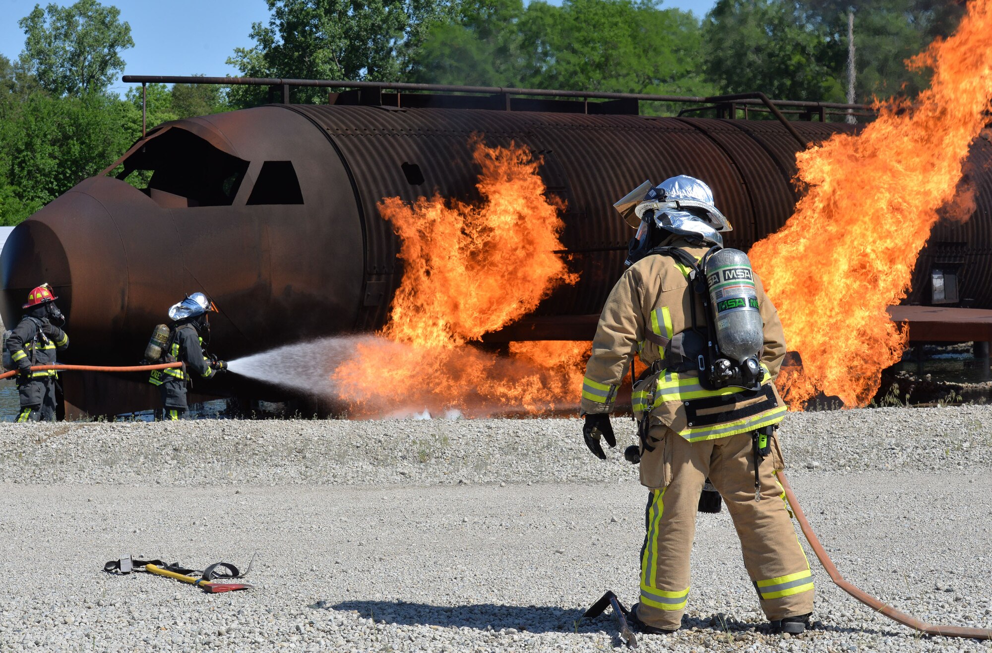 U.S. Air Force Brice Morgan, 788th Civil Engineer Squadron firefighter, stands-by, while fellow firefighters, Matthew Holley and Steven McKee, extinguish an aircraft fire, as part of annual proficiency skill training for firefighters, at their training burn pit, May 30, 2017, at Wright-Patterson Air Force Base, Ohio.  The team demonstrated their ability to extinguish aircraft and running fuel fires by using bumper turrets to attack the larger fire and using hand lines to go after spot fires. This helps allow aircraft crew and passengers to egress and for firefighters to rescue others incapacitated by smoke and other fire conditions. (U.S. Air Force photo/Michelle Gigante)