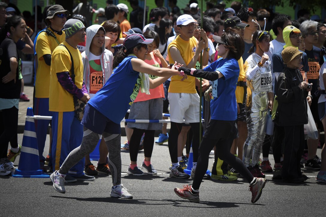 An Ekiden runner passes a sash to their relay teammate during the 33rd Annual Yokota Striders Ekiden Race at Yokota Air Base, Japan, June 4, 2017. An Ekiden is a Japanese long distance relay that consists of teams of runners covering a certain distance. The Yokota Ekiden is 20K in distance made up of four runners each running a 5K. (U.S. Air Force photo by Machiko Arita)