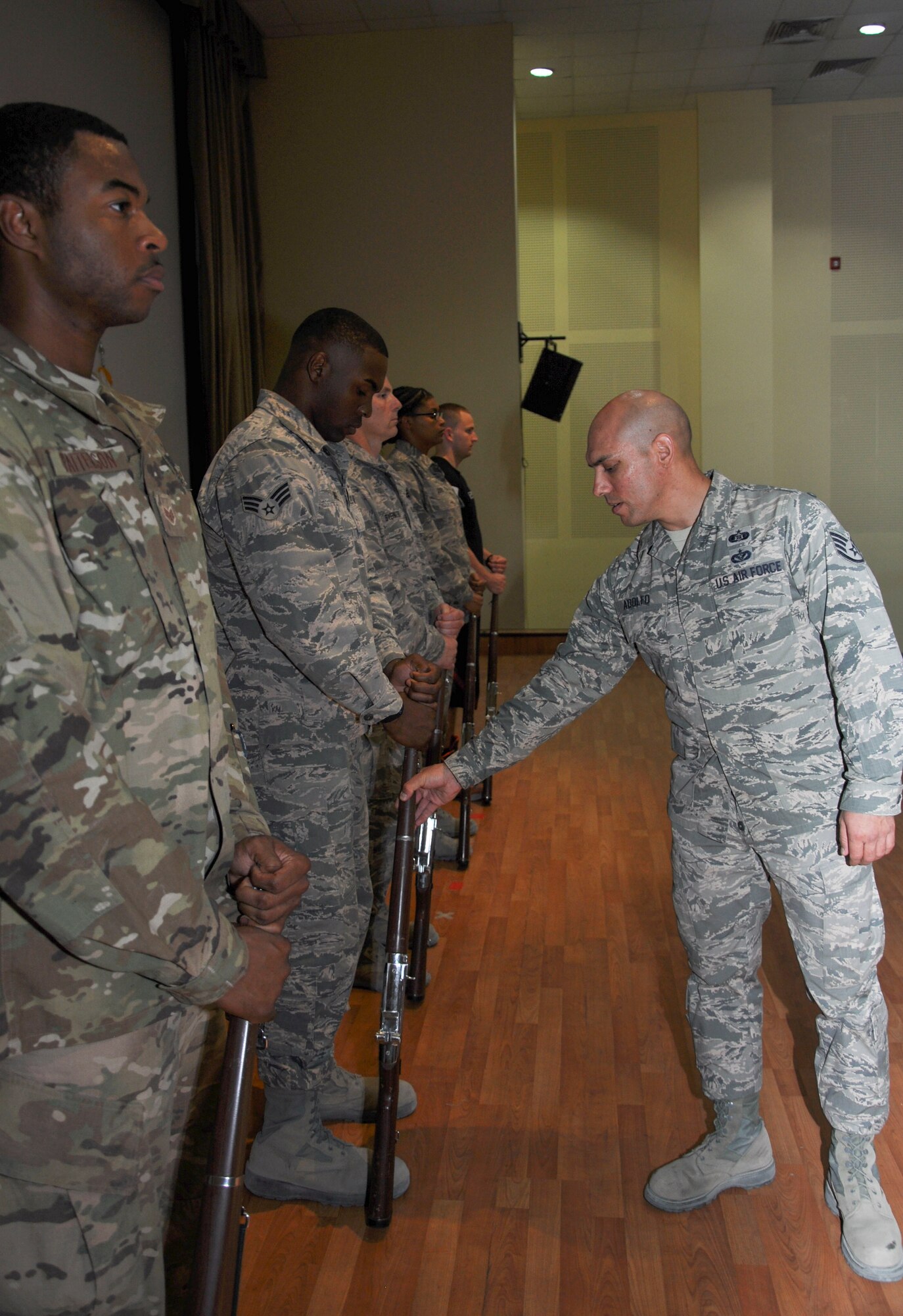 Staff Sgt. David Adolfo (right), honor guard trainer, makes an adjustment to the rifle position of Senior Airman Antonio Davis Tuesday, May 30, 2017, at the base theater at an undisclosed location in Southwest Asia. As team trainer, Adolfo leads the bi-weekly practice sessions the honor guard conducts on their personal time.