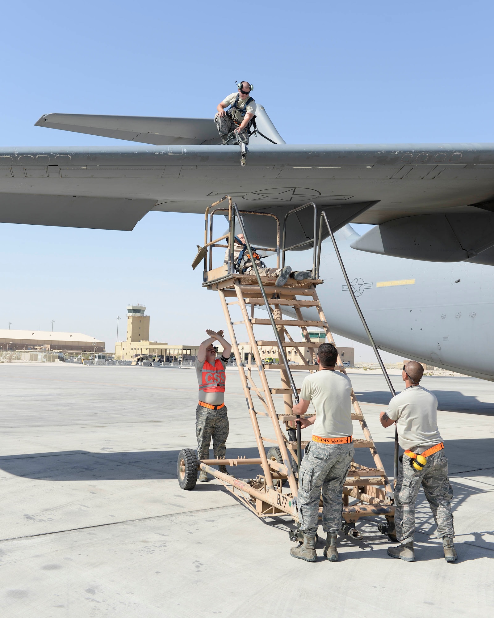 U.S. Air Force Airman 1st Class Jacob Trimble, guidance and control technician, looks on from the wing of a C-17 Globemaster III as Senior Airman Kyle Sherburne, communication and navigation technician, orange vest, guides Staff Sgts. Brett Rice, crew chief, left, and Gerardo Pesebre, Jr., repair and reclamation crew chief, right, as they move the rescue stairs into place during a fall protection exercise at Al Udeid Air Base, Qatar, June 6, 2017. The fall protection exercise was conducted by the members of the 8th Expeditionary Air Mobility Squadron in support of Fall Protection Awareness Month and was designed to test the 8 EAMS’ fall protection rescue plan. (U.S. Air Force photo by Tech. Sgt. Bradly A. Schneider/Released)