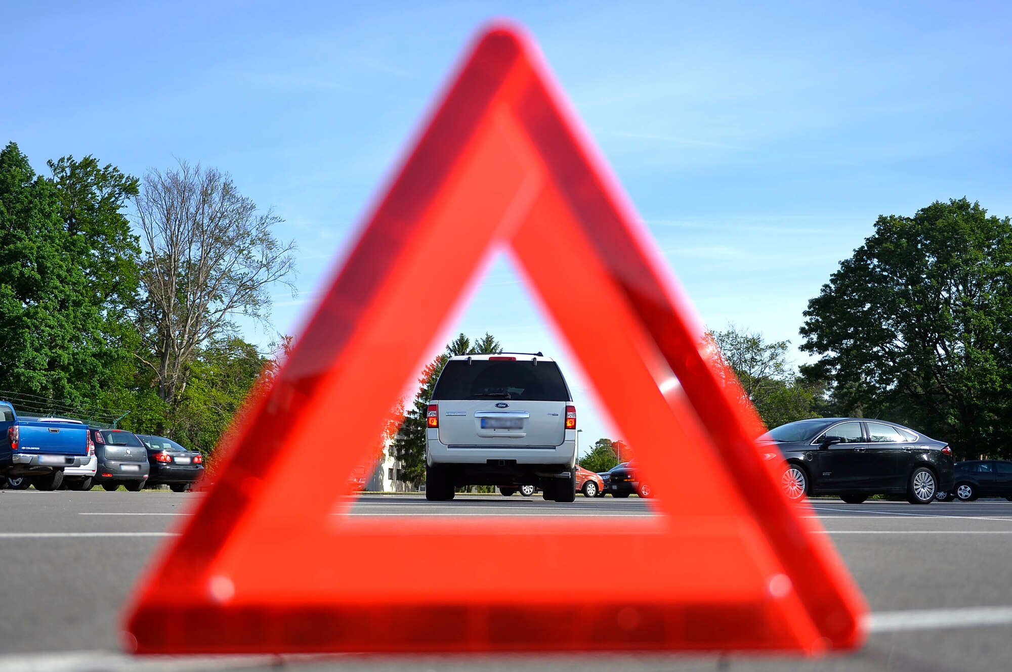 A hazard triangle stands behind a parked vehicle at Ramstein Air Base, Germany, June 8, 2017. Motorists in Germany are required to keep a first aid kit, reflective vests and a hazard triangle in their vehicle. (U.S. Air Force photo illustration by Airman 1st Class Joshua Magbanua)