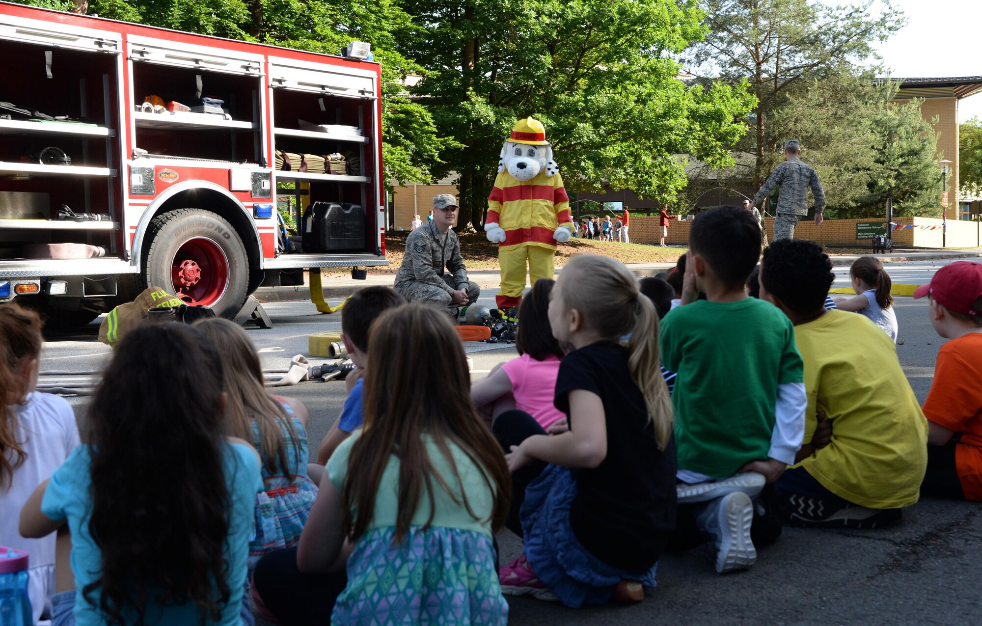 Staff Sgt. Joseph Bagnasco, 86th Civil Engineer Squadron firefighter, and Sparky, 86th Civil Engineer Squadron fire prevention mascot, explain the how firefighter gear is used at Ramstein Elementary School’s June Bug Out field day on Ramstein Air Base Germany, June 8, 2017. After a brief demonstration on how the firefighters use their gear students were allowed to take a visual tour of the fire truck. (U.S. Air Force photo by Airman 1st Class D. Blake Browning)