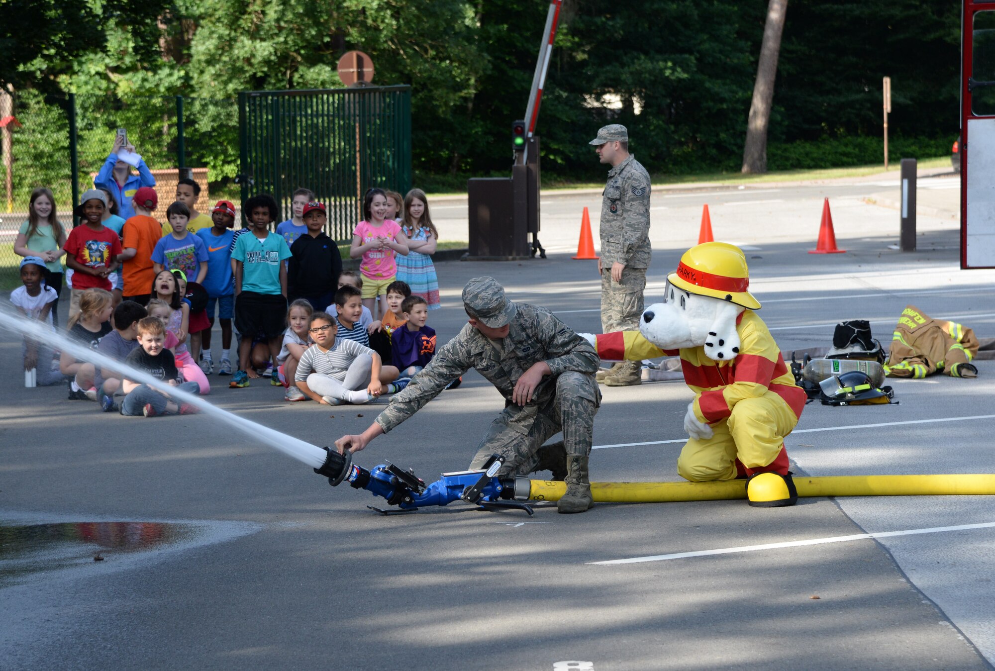 Sparky, 86th Civil Engineer Squadron fire prevention mascot, extends emotional support to Airman 1st Class Derek Kildow, 86th Civil Engineer Squadron firefighter, as he demonstrates how to use a fire extinguisher at Ramstein Elementary School’s June Bug Out field day on Ramstein Air Base, Germany, June 8, 2017. 10 CES Airmen volunteered at the field day to show students a portion of their day to day activities as firefighters. (U.S. Air Force photo by Airman 1st Class D. Blake Browning) 