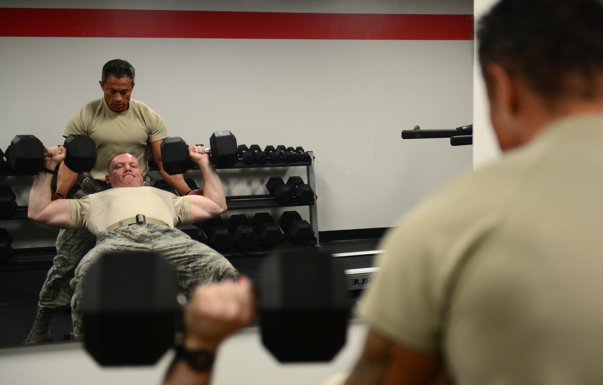 U.S. Air Force Tech. Sgt. Ricardo Zuniga, a weapons load crew member from the 131st Aircraft Maintenance Squadron, spots U.S. Air Force Master Sgt. Jonathon Hamilton, a weapons load crew member from the 131st Aircraft Maintenance Squadron, while he performs dumbbell presses at Whiteman Air Force Base, Mo., May 30, 2017. The flightline gym was recently renovated to benefit flightline personnel wanting to get a workout in without having to leave the flightline. (U.S. Air Force photo by Senior Airman Joel Pfiester)
