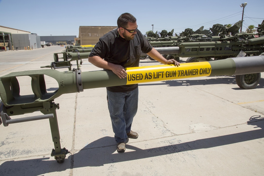 David Vierheller, artillery repair specialist, stands by the portion of the barrel of a M777 lift gun trainer bearing the sign reminding users the gun is not operable and is only used for training helicopter pilots and their rigging crews how to transport the howitzer by air.