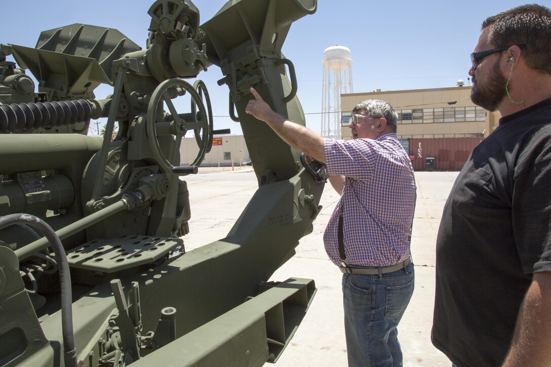 (Left) Doug Van Dyke, artillery supervisor, Production Plant Barstow, Marine Depot Maintenance Command, points out the sighting mechanism on the M777 lift gun. He said the crews that rig the sling to the underside of a helicopter to transport the howitzer by air, have to remove the sights or they will break off from pressure of the sling cables.