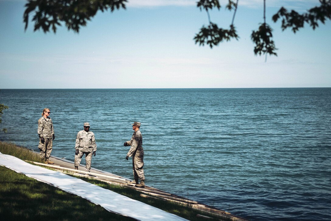 New York Air National Guard Tech Sgt. Jamie Groff, left, and Master Sgt. Joe Elder, center, and Staff Sgt. James McCormick lay out materials to build a preventative barrier along an eroded shoreline on a local home owner’s property in Wilson, N.Y., June 9, 2017. Air National Guard photo by Staff Sgt. Ryan Campbell