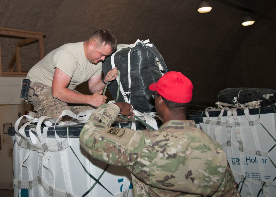Spc. Alexander Triska and Spc. Keith Manning of the 824th Quartermaster Company, secure a parachute to a container for aerial delivery at Al Udeid Air Base, Qatar on April 25, 2017. Aerial delivery operations are essential for getting supplies to troops in the Middle East when conventional means of transportation are not feasible. (U.S. Army photo by Sgt. Jeremy Bratt)