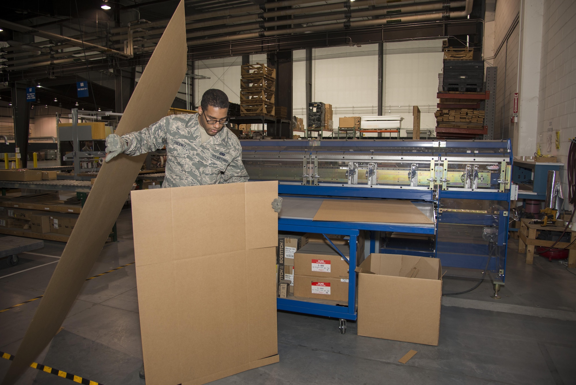 Senior Airman Gerard Pinckney, 436th Aerial Port Squadron traffic management specialist, picks up a piece of cardboard ready to be installed into a box Jan. 12, 2017, at the aerial port on Dover Air Force Base, Del. Making boxes as needed reduces the amount of storage space required, limits the amount of materials that need to be stored and reduces material waste. (U.S. Air Force photo by Senior Airman Aaron J. Jenne)