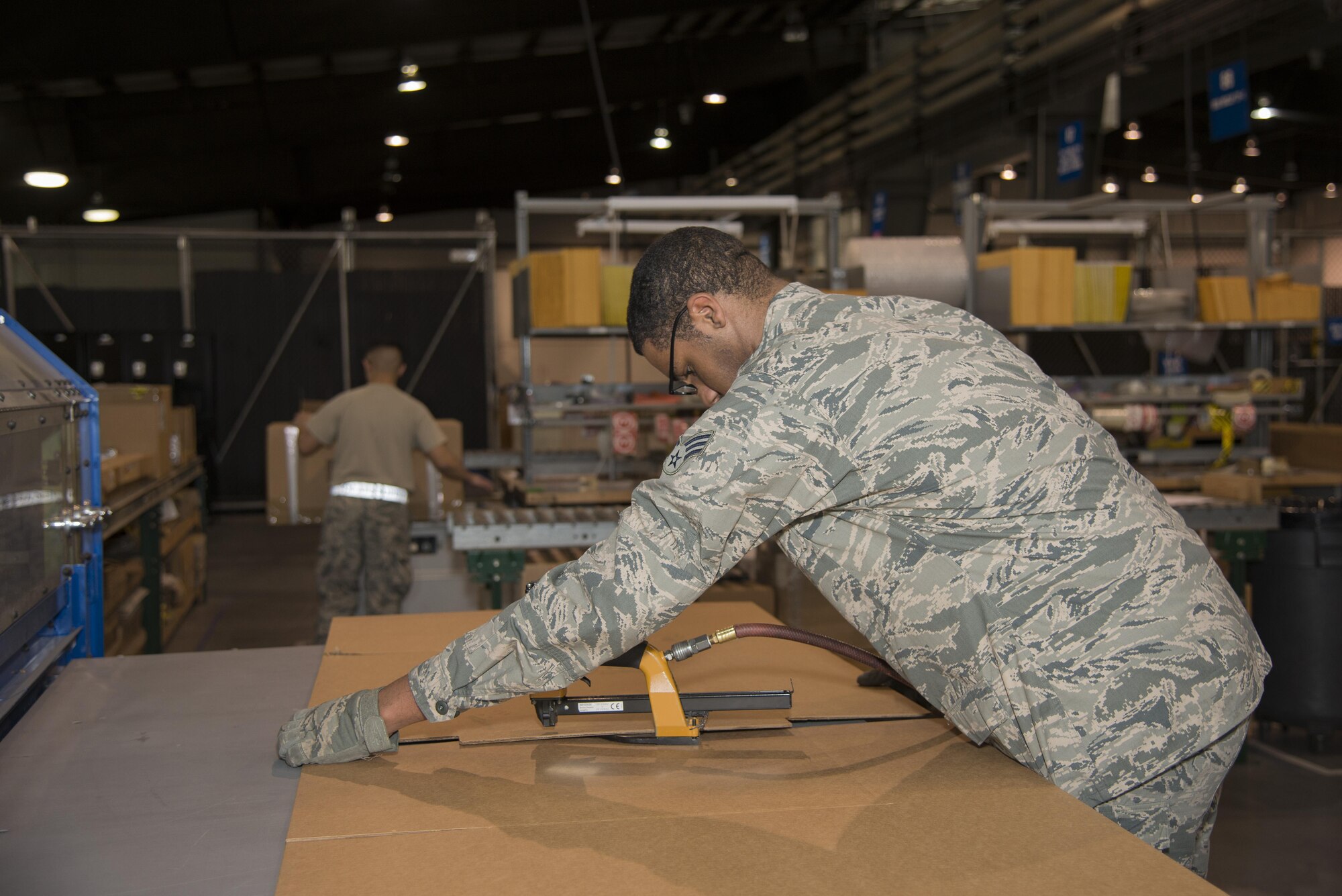 Senior Airman Gerard Pinckney, 436th Aerial Port Squadron traffic management specialist, staples two pieces of a cardboard box together Jan. 12, 2017, at the aerial port on Dover Air Force Base, Del. Using the box-making machine, Airmen can calculate dimensions and create a shipping box in only a few minutes. (U.S. Air Force photo by Senior Airman Aaron J. Jenne)