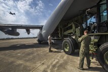 A B-24 Liberator flies over as aerial porters with the 35th Aerial Port Squadron, 514th Air Mobility Wing, work with a loadmaster in directing a loader during an engine running exercise on a CW-130 Hercules with the 53rd Weather Reconnaissance Squadron at the Combat Readiness Training Center at Gulfport, Miss., in support of Crisis Response '17 March 5, 2017. Close to 700 Air Mobility Command Airmen with the 514th Air Mobility Wing, the 305th Air Mobility Wing, the 87th Air Base Wing, and the 621st Contingency Response Wing are participating in the mobilization exercise. (U.S. Air Force photo by Master Sgt. Mark C. Olsen/Released)