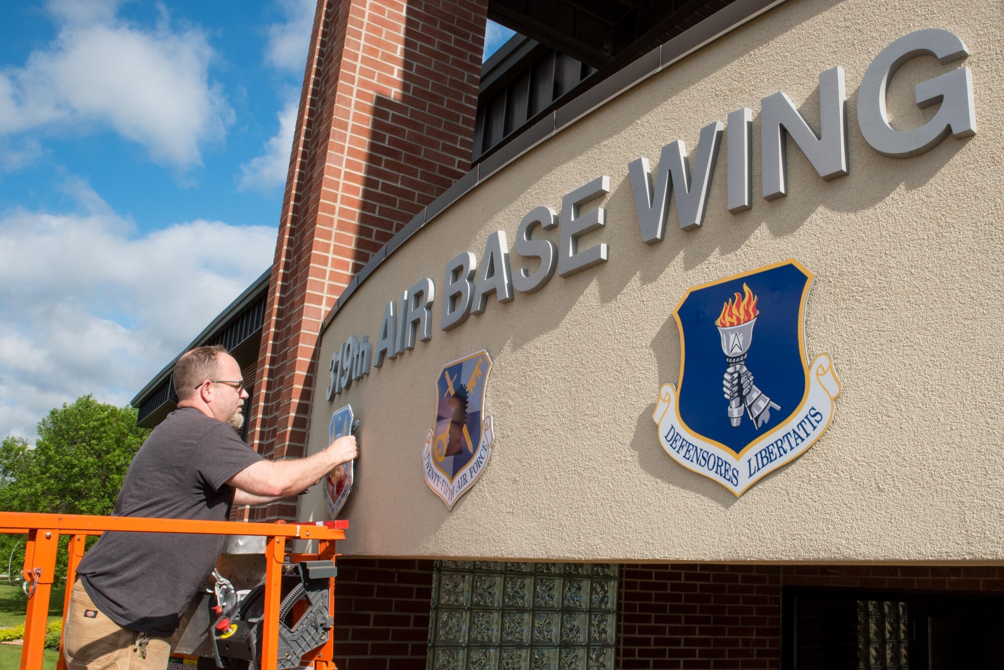 Michael J. Hafstad, a maintanence mechanic with the 319th Civil Engineering Squadron installs the Air Combat Command shield over the wing headquarters building June 14, 2017, on Grand Forks AFB, N.D.  The base underwent a realignment from the Air Mobility Command to Air Combat Command effective June 13, 2017. (U.S. Air Force photo by Master Sgt. Eric Amidon)