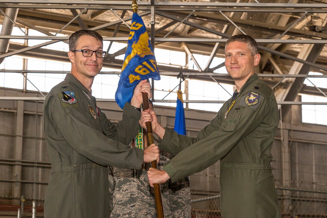 Col. Scott Cain, 412th Operations Group commander (left), and Lt. Col. Tucker Hamilton, the new commander of the 461st Flight Test Squadron, pose for a photo with the squadron’s guidon June 9 in Hangar 1830. Hamilton assumed command of the squadron, which oversees developmental testing of the F-35 Joint Strike Fighter. (Courtesy photo by Darin Russell/Lockheed Martin)