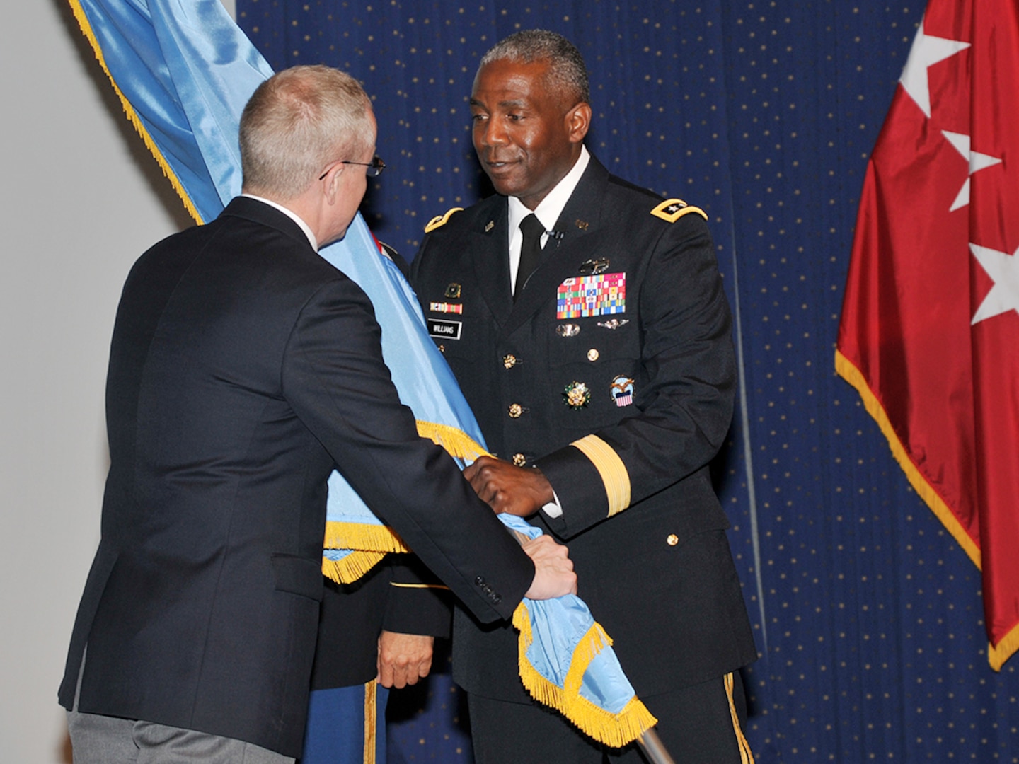 James MacStravic, performing the duties of the under secretary of defense for acquisition, technology and logistics, passes the Defense Logistics Agency command flag to the agency's new director, Army Lt. Gen. Darrell Williams.