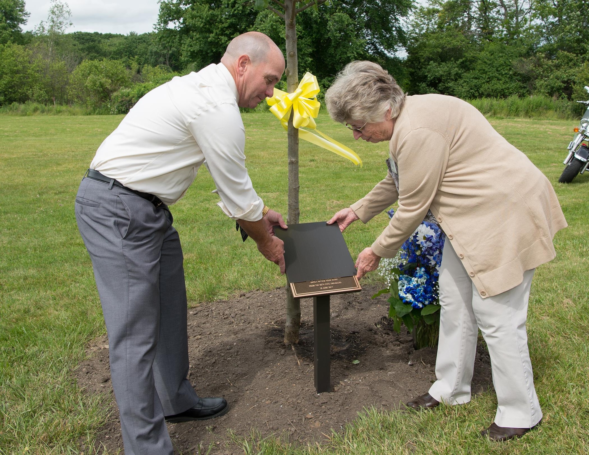 Jackie Guthrie unveils a plaque in memory of her late husband, Dennis “Dennie” Guthrie, with help from Steve Schofield, a member of the 66th Civil Engineering Division, during a Memorial Park Dedication Ceremony at Hanscom Air Force Base, Mass., June 16. Guthrie worked for the 66th Civil Engineering Division as a heating, ventilation and air conditioning technician. Also honored during the event were Dana E. Kirane and retired Tech. Sgt. John A. Raynes. (U.S. Air Force photo by Jerry Saslav)