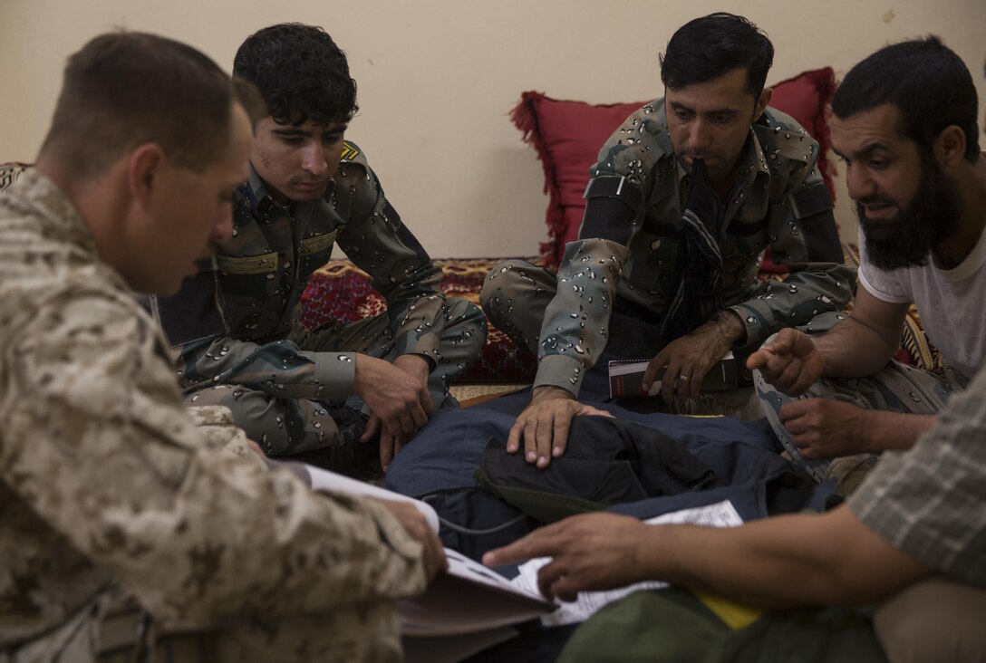 A U.S. Marine advisor with Task Force Southwest, left, highlights important pieces of information with the 505th Zone National Police engineers about utilizing the EOD9 bomb suit during a mission at Bost Airfield, Afghanistan, June 13, 2017. During the class, the advisor discussed the specifications of the suit, as well as how to properly clean and maintain it. Utilizing the bomb suit will help the engineers safely and efficiently remove improvised explosive device threats and help maintain security for the local populace.  Task Force Southwest, comprised of approximately 300 Marines and Sailors from II Marine Expeditionary Force, are training, advising and assisting the Afghan National Army 215th Corps and the 505th Zone National Police. (U.S. Marine Corps photo by Sgt. Justin T. Updegraff)