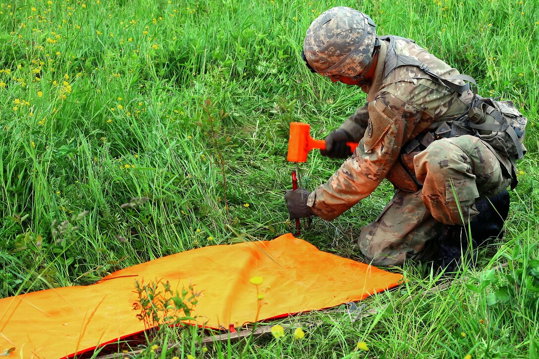 New York Army National Guard Pfc. Nicholas Timbrouck places a panel to mark the landing zone for a UH-60 Black Hawk helicopter during an air assault artillery raid at Fort Drum, N.Y., June 9, 2017. Timbrouck is a cannon crewmember assigned to Alpha Battery, 1st Battalion, 258th Artillery Regiment, 27th Infantry Brigade Combat Team. Army National Guard photo by Sgt. Alexander Rector