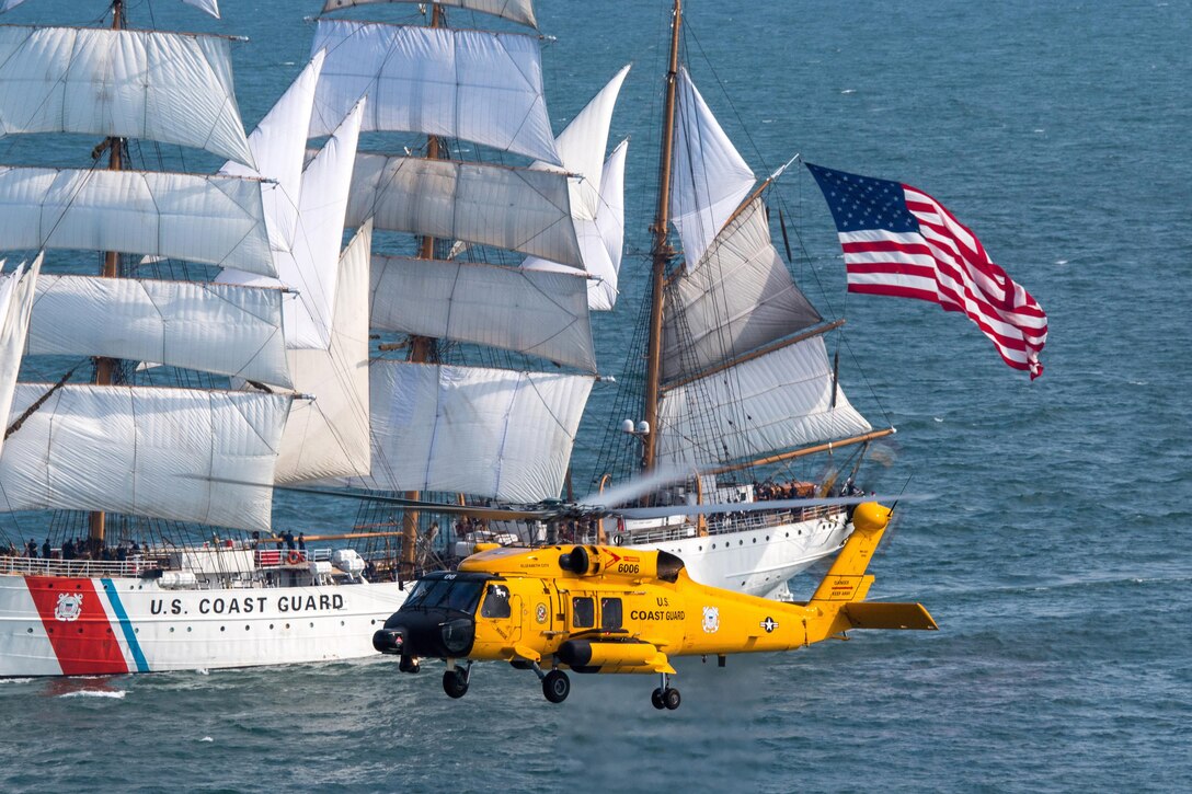 A Coast Guard MH-60 Jayhawk helicopter flies beside the Coast Guard Cutter Eagle in Norfolk, Va., June 12, 2017. U.S. Coast Guard Academy cadets train aboard the Eagle to learn historic aspects of sailing, leadership, navigation and teamwork. Coast Guard photo by Auxiliarist David Lau