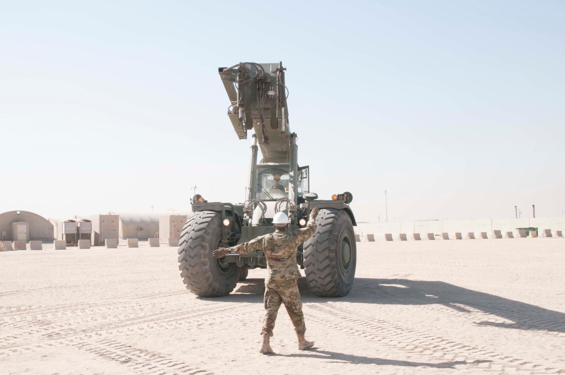 U.S. Army Master Sgt. Edgar Ponce guides Spc. Agnes Torres, both with the 369th Sustainment Brigade, as she drives a Rough Terrain Container Handler (RTCH) at Camp Arifjan, Kuwait, on November 12, 2016. RTCHs are used to move large containers over various types of terrain. (U.S. Army photo by Sgt. Jeremy Bratt)