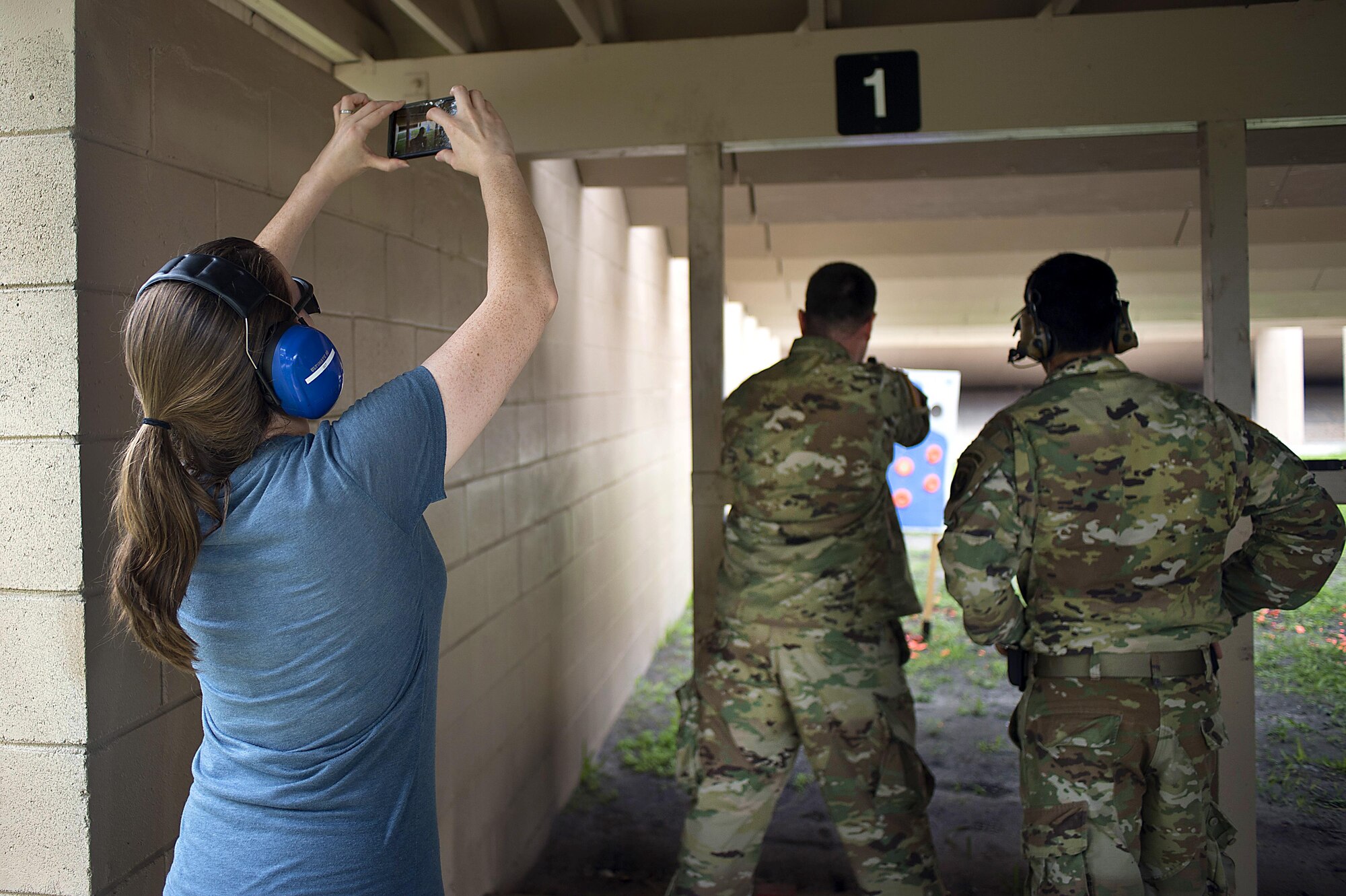 Christie Patterson, the wife of a Special Operations Command Central (SOCCENT) service member, takes a photo of her husband firing a handgun during Spartan Spouse Day at MacDill Air Force Base, June 13, 2017. During the day, spouses of SOCCENT members learned how to properly load, fire and unload a handgun. (U.S. Air Force photo by Airman 1st Class Caleb Nunez)