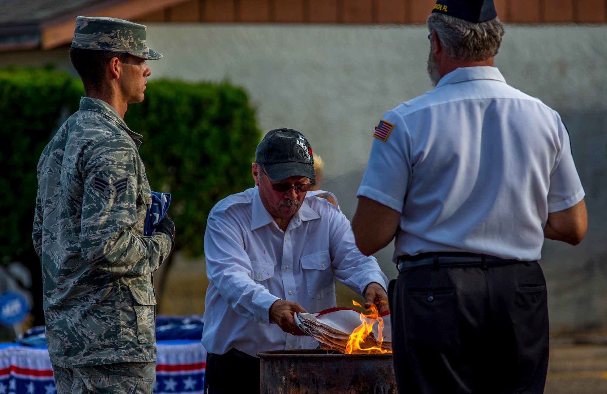 Senior Airman Anthony Padilla, 96th Aircraft Maintenance Squadron, prepares to place the remnants of the worn flag into a bonfire with American Legion members, during a ceremony held on Flag Day, June 14. The most accepted manner is to cut the blue field of stars from the red and white stripes, thereby rendering it no longer a flag. The remaining pieces are then placed into in a fire. When a flag is worn beyond repair, it is retired in a dignified manner. (U.S. Air Force photo/Kristin Stewart)