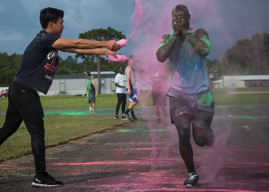 A runner covers his face as Airman 1st Class Carladrien Aguilar, volunteer from the 96th Logistics Readiness Squadron, squeezes a container of colored chalk at him during the LGBT Pride Month 5K Color Run June 14 at Eglin Air Force Base, Fla. The run was held to celebrate diversity and to raise inclusion awareness. (U.S. Air Force photo/Ilka Cole)