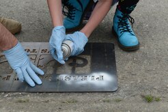 Kerbi Flood, 11, daughter of Tech. Sgt. Joshua Flood, 673d Civil Engineer Squadron, spray paints the first new design in front of the storm drain by Ursa Major Elementary school with help from Dwayne Ray, toxics and water program manager, at Joint Base Elmendorf-Richardson, June 6, 2017. Local schools hosted a competition for a new design in front of storm drains to deter pollution and hers won of an octopus behind bars. 