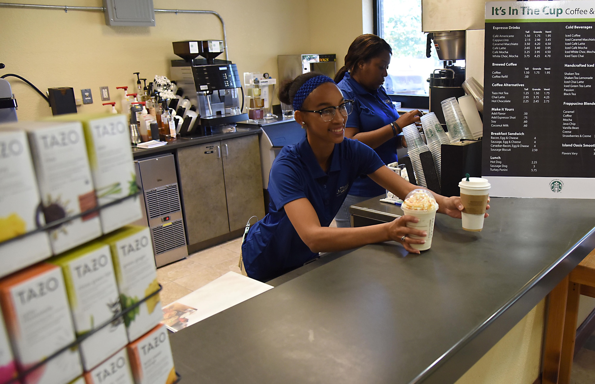 Quiana James and Teaunda Rodgers, 81st Force Support Squadron sales clerks, serve and prepare orders at “It Is In The Cup” in the Bay Breeze Event Center June 8, 2017, on Keesler Air Force Base, Miss. Keesler's new coffee & smoothie bar will have its grand opening on June 29 at the Bay Breeze Event Center. The facility proudly serves Starbucks coffee, Frappuccino’s, iced beverages and espresso as well as Island Oasis smoothies in a variety of flavors. A full menu of items can be found at keesler81fss.us. (U.S. Air Force photo by Kemberly Groue)