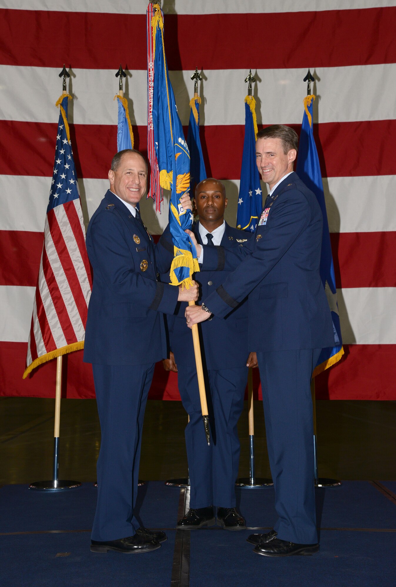 Air Force Sustainment Center Commander Lt. Gen. Lee K. Levy II passes the Oklahoma City Air Logistics Complex guidon to Brig. Gen. Tom D. Miller during a change of command ceremony at Bldg. 9001 June 16. Master Sgt. Teodros Rembert, OC-ALC first sergeant, serves as guidon bearer. Miller will lead a 9,800 personnel team responsible for $3 billion in revenue. (Air Force photo by Kelly White)