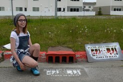 Kerbi Flood, 11, daughter of Tech. Sgt. Joshua Flood, 673d Civil Engineer Squadron, spray painted the first new design in front of the storm drain by Ursa Major Elementary school at Joint Base Elmendorf-Richardson, June 6, 2017. Local schools hosted a competition for a new design in front of storm drains to deter pollution and hers won of an octopus behind bars. 