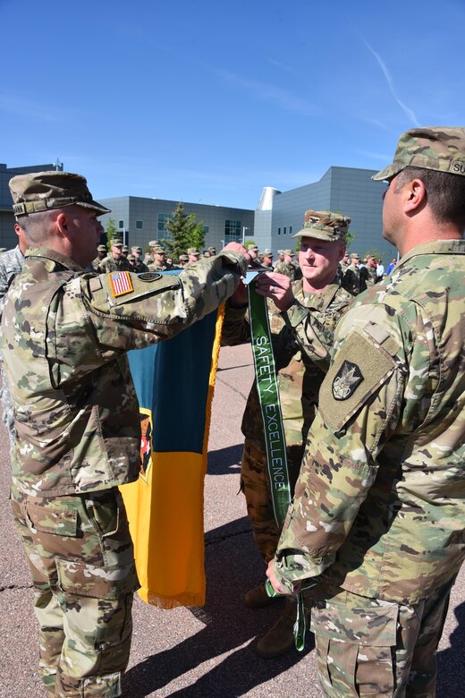 PETERSON AIR FORCE BASE, Colorado --Col. Rick Zellmann (left), 1st Space Brigade commander, assists as Col. Tim Lawson (right), deputy commander for Operations, U.S. Army Space and Missile Defense Command/Army Forces Strategic Command, awards the 2016 Army Safety Excellence Streamer to the 1st Space Brigade during Stand-up for Safety Day, June 8, at the Peterson Air Force Base, Colo., headquarters.  Also pictured is Command Sgt. Maj. Scott Sutherland, 1st Space Brigade command sergeant major. (U.S. Army photo by Dottie White)